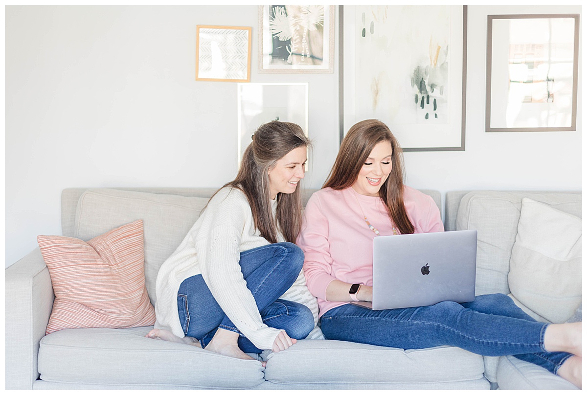 two women working on a computer while sitting on a couch